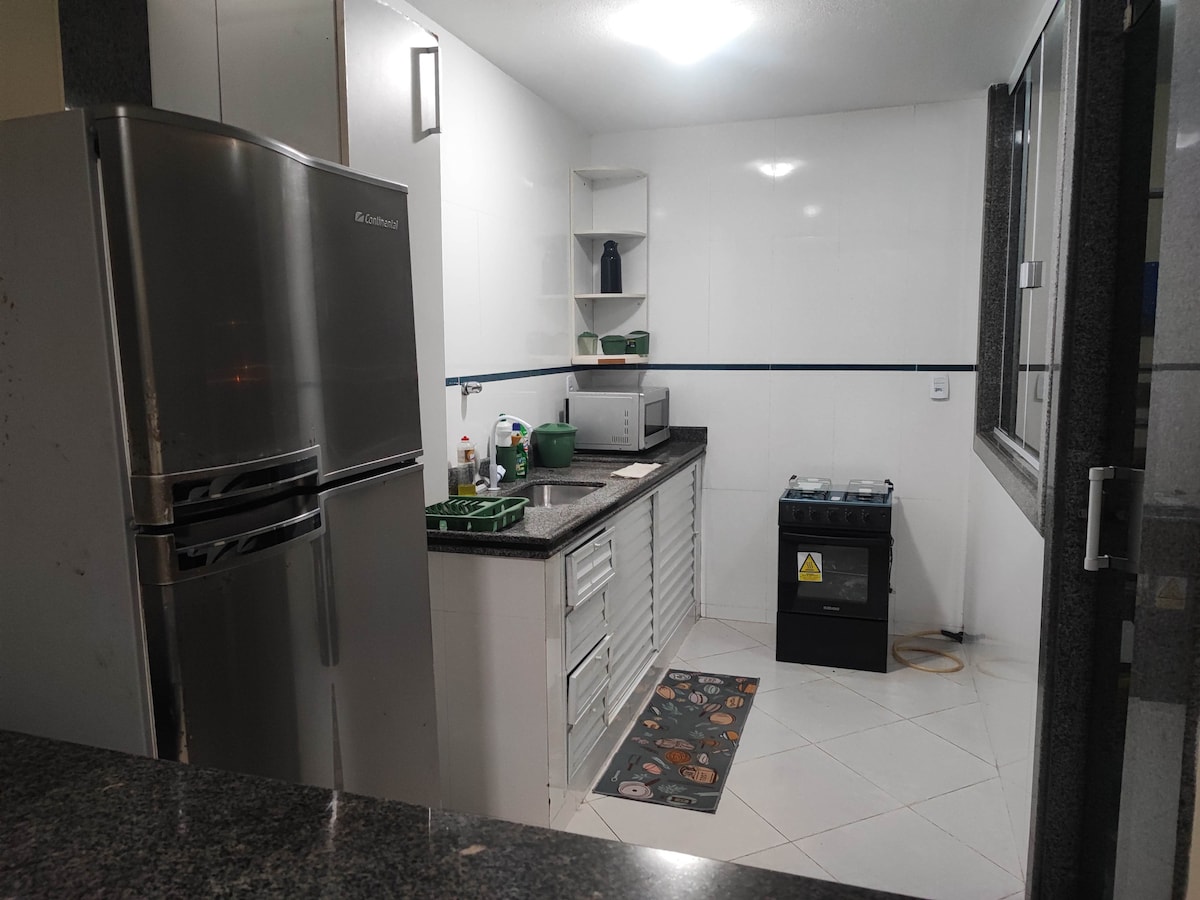 A functional kitchen area is depicted, featuring modern appliances including a stainless steel refrigerator, a microwave, and a stove. The countertop is complemented by ample storage cabinets. A patterned mat adds a touch of detail to the tiled floor, while large windows provide natural light.