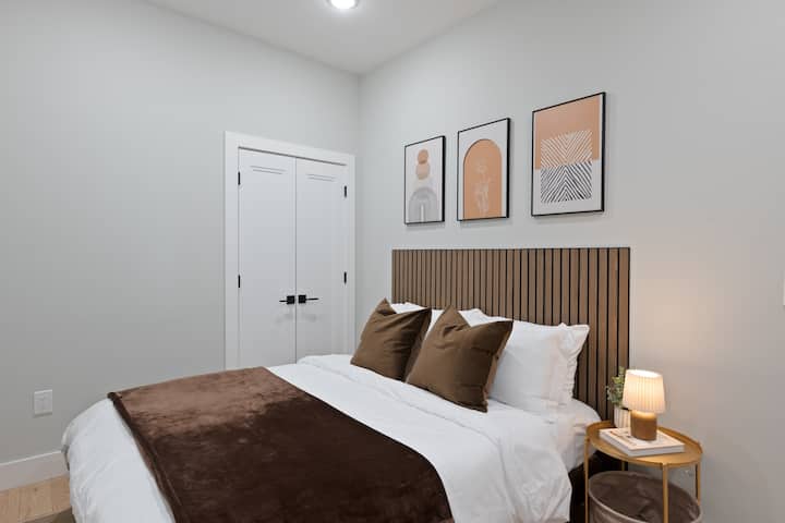 Veľká manželská posteľ so zvýrazneným panelom ako čelo postele. Televízor namontovaný na druhej strane steny nie je viditeľný. 