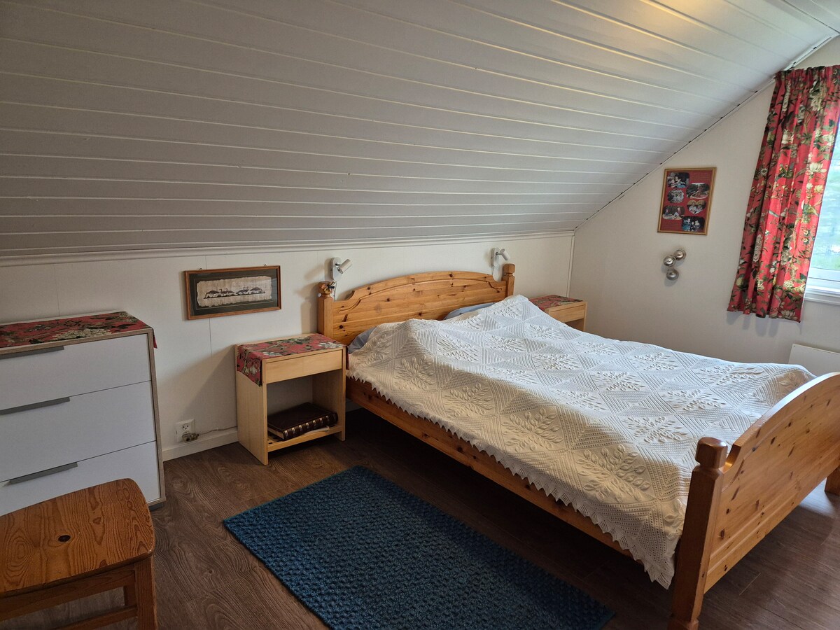 غرفة نوم مواجهة للغرب بسرير مزدوج بعرض 150 سم وألحفة بطول 220 سم. منضدتان ومصباحان.