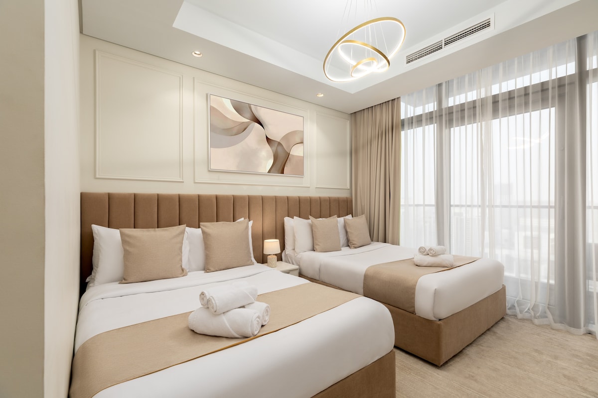 Софистицирана спална соба со топли неутрални тонови, дизајнерско осветлување и директен пристап до приватен балкон со поглед на центарот на Дубаи и Бурџ Калифа.
