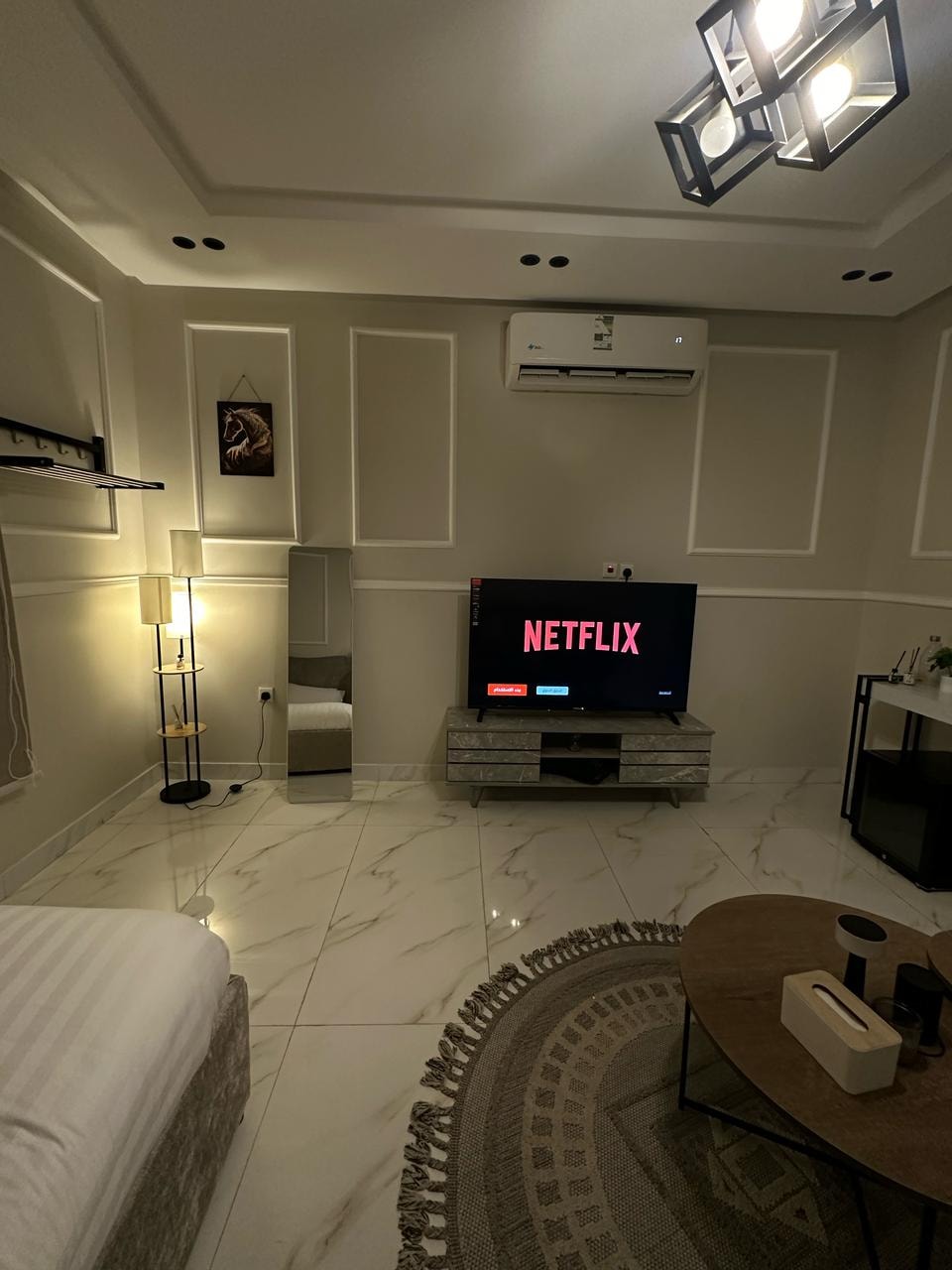 A living area is presented with a sleek television displaying Netflix, complemented by a stylish coffee table and a cozy rug. Light fixtures add a modern touch, while neutral walls and polished flooring create a sophisticated environment.