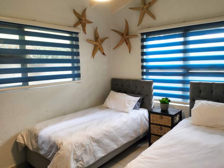 Terza camera da letto: due letti singoli con biancheria da letto oversize, armadi generosi e arredamento costiero personalizzato. Matite colorate e carta invitano i più piccoli a trascorrere giornate creative e accoglienti al chiuso.