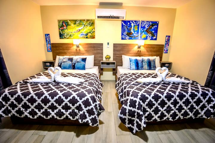 חדר שינה גדול עם 2 מיטות קווין סייז, מגבות ברבור, מזגן, מאוורר תקרה, שקעי USB, יצירות אמנות מקומיות בהתאמה אישית. 