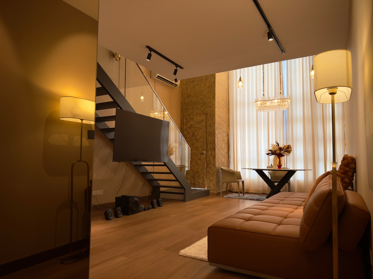A spacious living area features a comfortable sofa and a contemporary dining table, illuminated by soft lighting. A stylish staircase leads to an upper level, while large windows dressed in elegant curtains allow for natural light to fill the space.