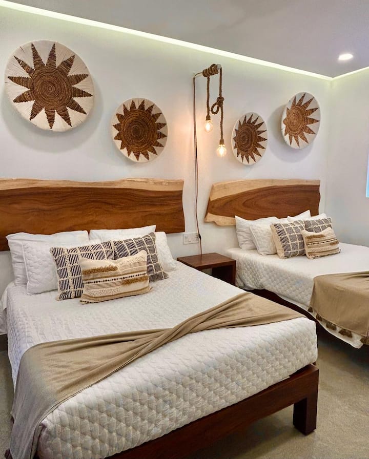 Одморете се во оваа соба со природен и модерен стил. Има два брачни кревета со дрвени потпирачи за глава, рачно изработен текстил и пријатно осветлување. Декорацијата со ткаени парчиња и детали во неутрални тонови даваат чувство на хармонија.