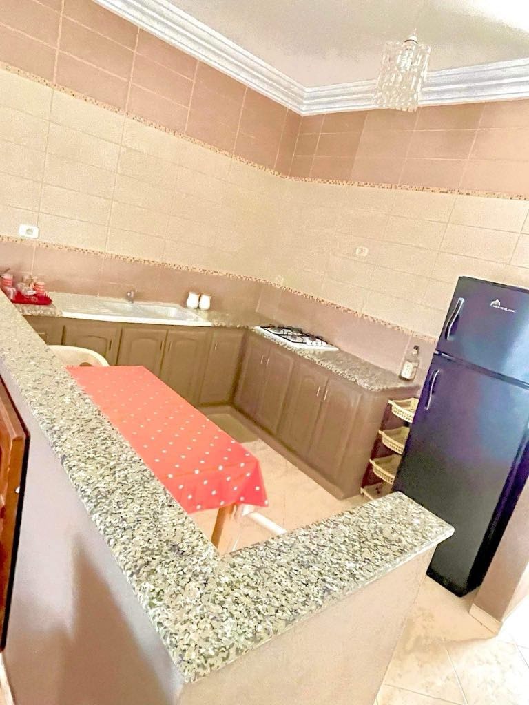 A compact kitchen space features light-colored cabinetry with a granite countertop. A small red table with white polka dots is positioned near the sink, enhancing the practicality of the area. A black refrigerator stands in the corner, contributing to the overall functionality.