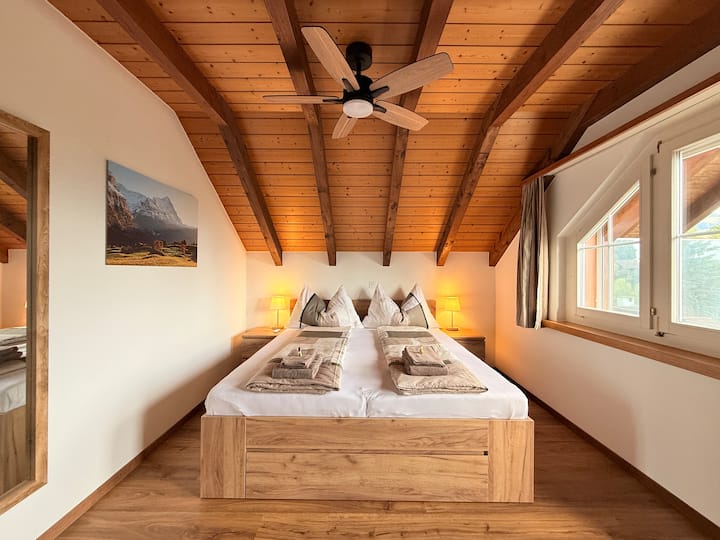 Cama doble grande y nueva (julio de 2025) con somier de láminas ajustable y colchones de muelles ensacados, 180 x 200 cm - cama tamaño «king»; ventilador de techo más ventilador de pie adicional, armario y cómodas. Dormitorio con vistas a Thun y las montañas