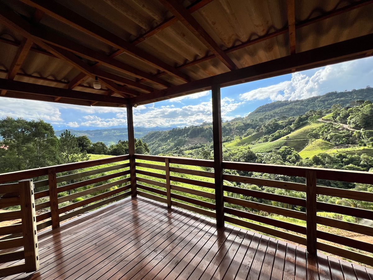 A spacious wooden deck is presented with a roof, showcasing expansive views of rolling hills and lush greenery. The clean lines of the railing complement the natural landscape, while wooden flooring adds warmth to the outdoor space.