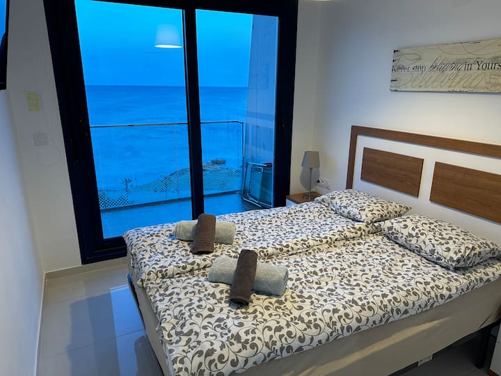 გაიღვიძეთ ხმელთაშუა ზღვის ხედით — ნათელი და წყნარი მთავარი საძინებელი, რომელსაც ტერასაზე გამავალი მოცურების კარი აქვს. ზღვის ფანტასტიკური ხედი.