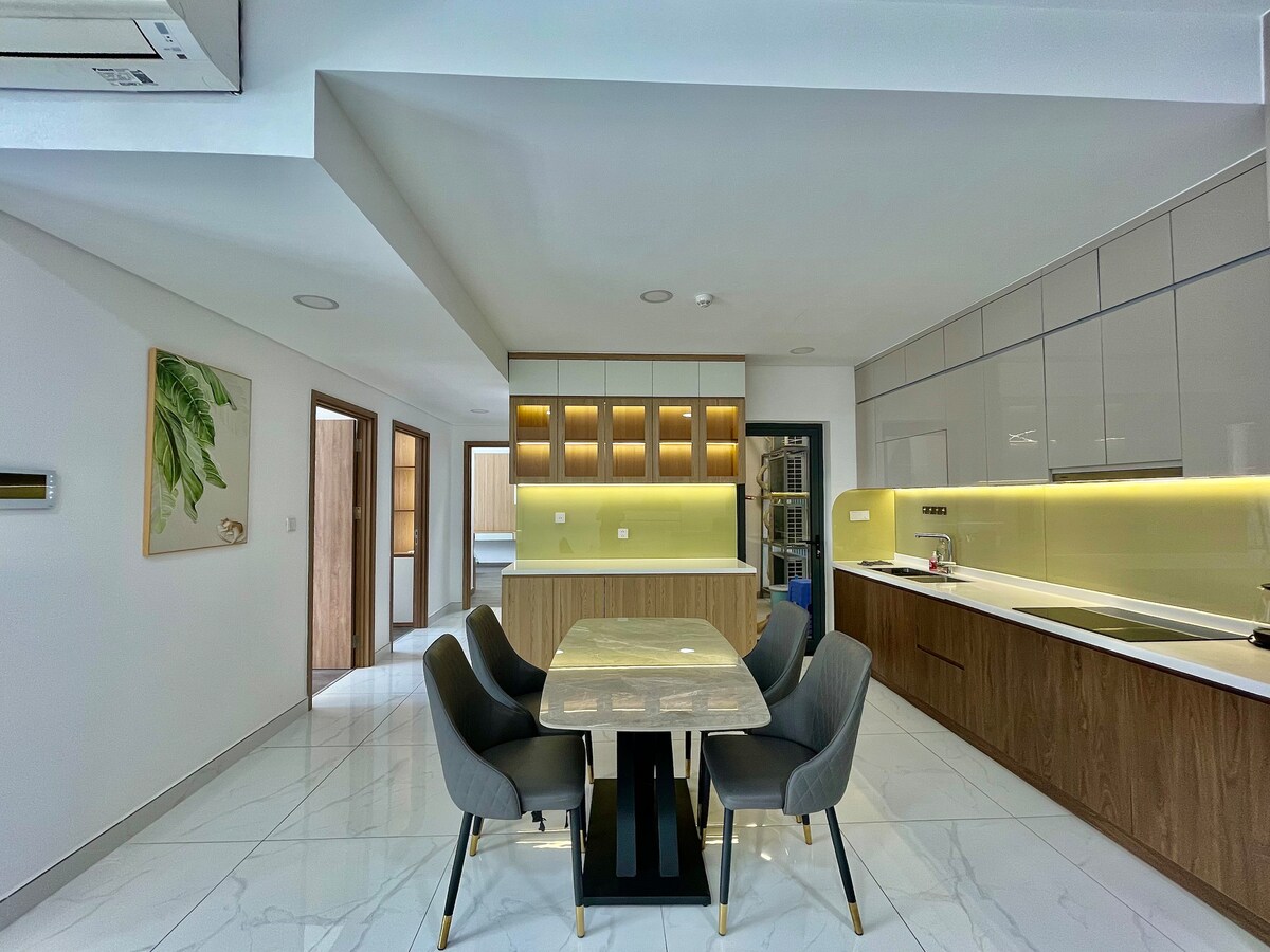 A modern kitchen area is depicted, featuring sleek cabinetry and a large dining table surrounded by comfortable chairs. Soft lighting highlights the countertops, while a subtle backsplash adds texture. The open layout allows for seamless flow towards adjoining spaces.