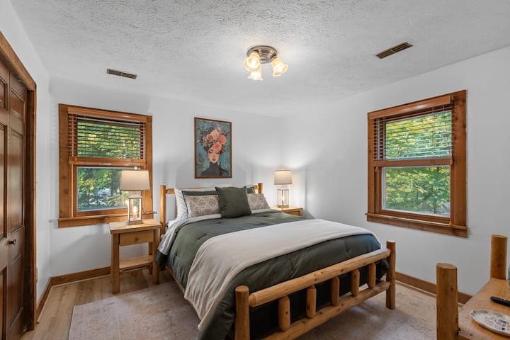 Chumba cha kulala chenye starehe kilicho na kitanda cha mbao cha ukubwa wa kifalme kilichotengenezwa kwa mikono, mapambo ya mbao ya joto na mwonekano wa dirisha la majani kwa ajili ya mapumziko ya usiku yenye amani.