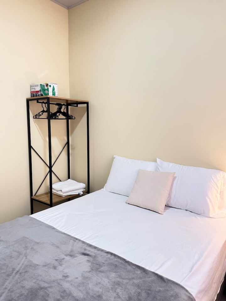 Kitanda cha watu wawili, taulo mbili, kioo, kabati la chuma, pasi, feni na meza ya kuweka taa.