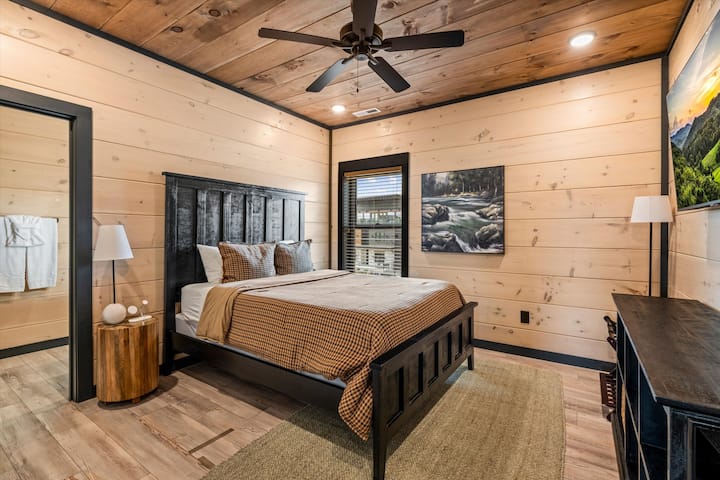 Cozy rustic bedroom with wood ceilings, ensuite access, and lodge-style charm