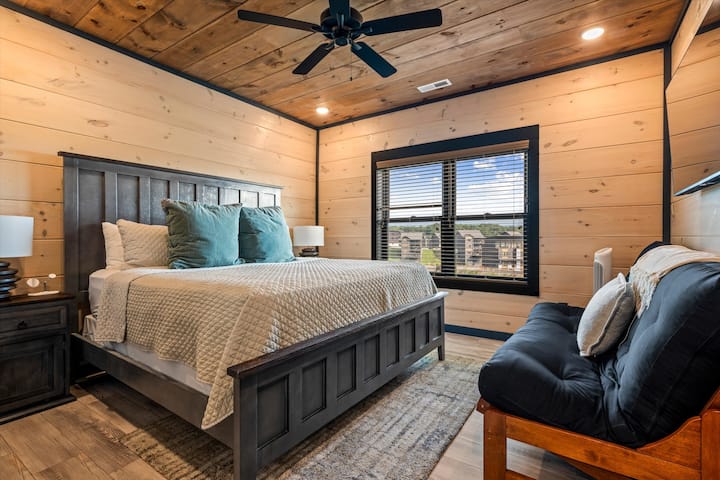 Cozy wood-paneled bedroom with plush king bed, futon, and natural light