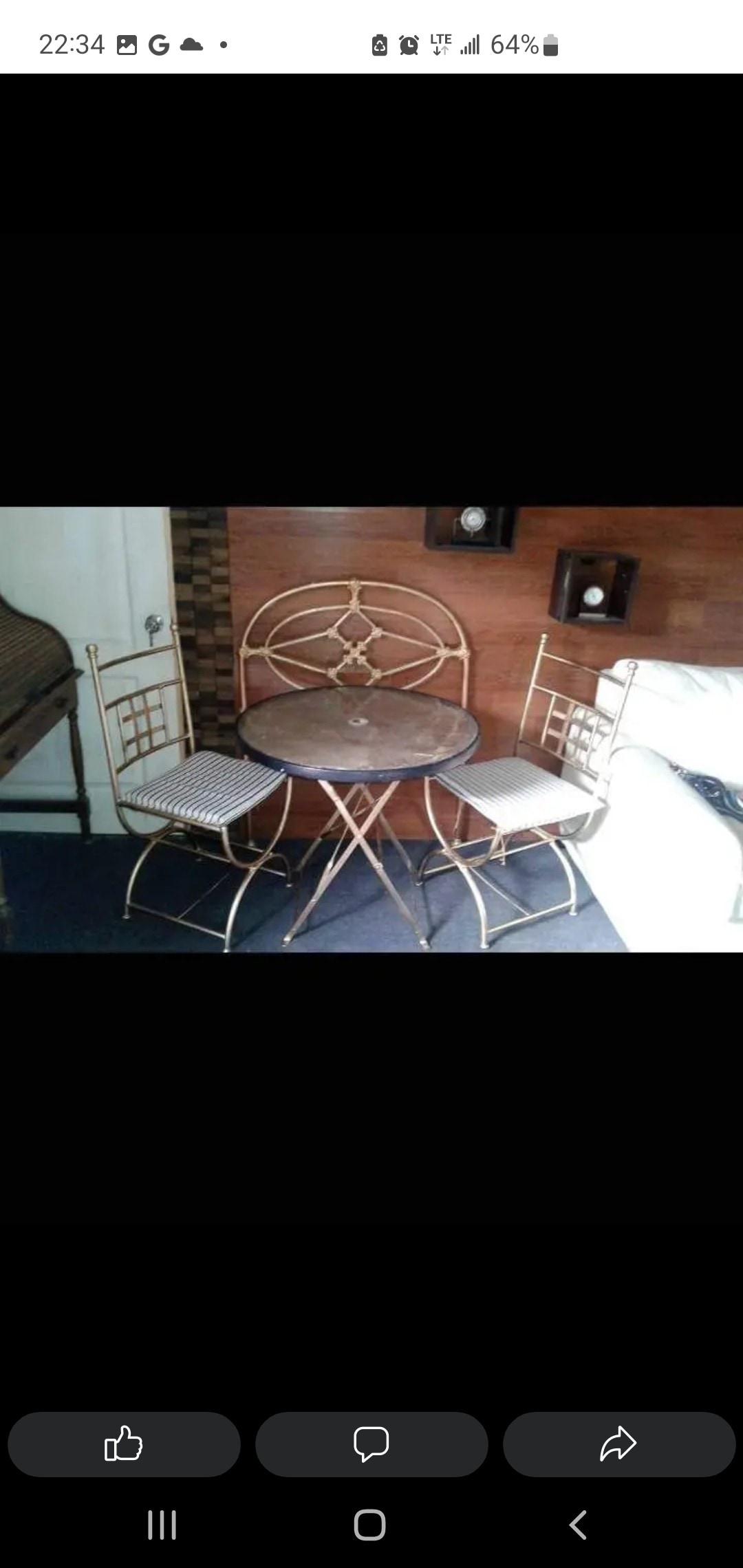 A small dining set is featured, consisting of a round table and two chairs. The table has a patterned surface, and the chairs are designed with a woven seat. The arrangement is situated in a cozy corner, with wood paneling visible in the background.