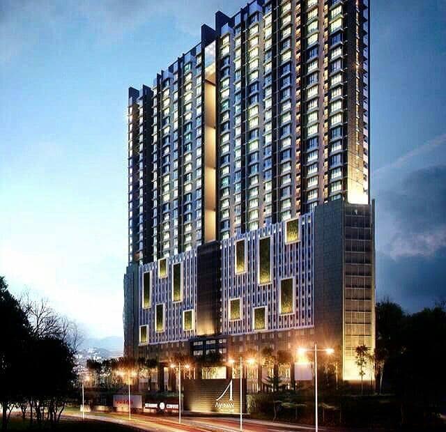 The exterior of a high-rise condominium is illuminated at dusk, showcasing a modern architectural design. The building features rows of windows, with warm lights contrasting against the evening sky. Surrounding greenery and street elements contribute to an inviting city atmosphere.