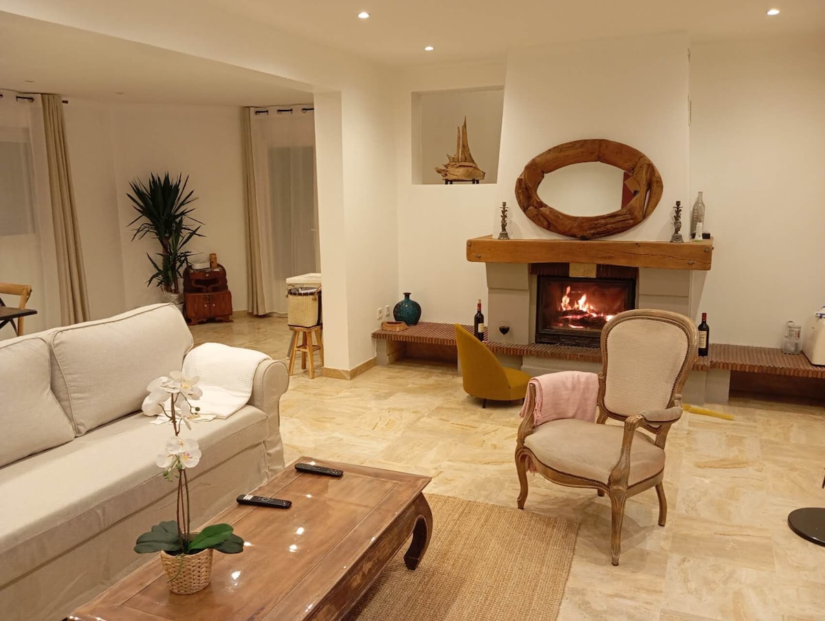 A spacious living area is presented, featuring a light-colored sofa and wooden coffee table. A fireplace with a wooden mantel serves as a focal point. Soft lighting adds warmth, while decorative items and a plant enhance the inviting ambiance.