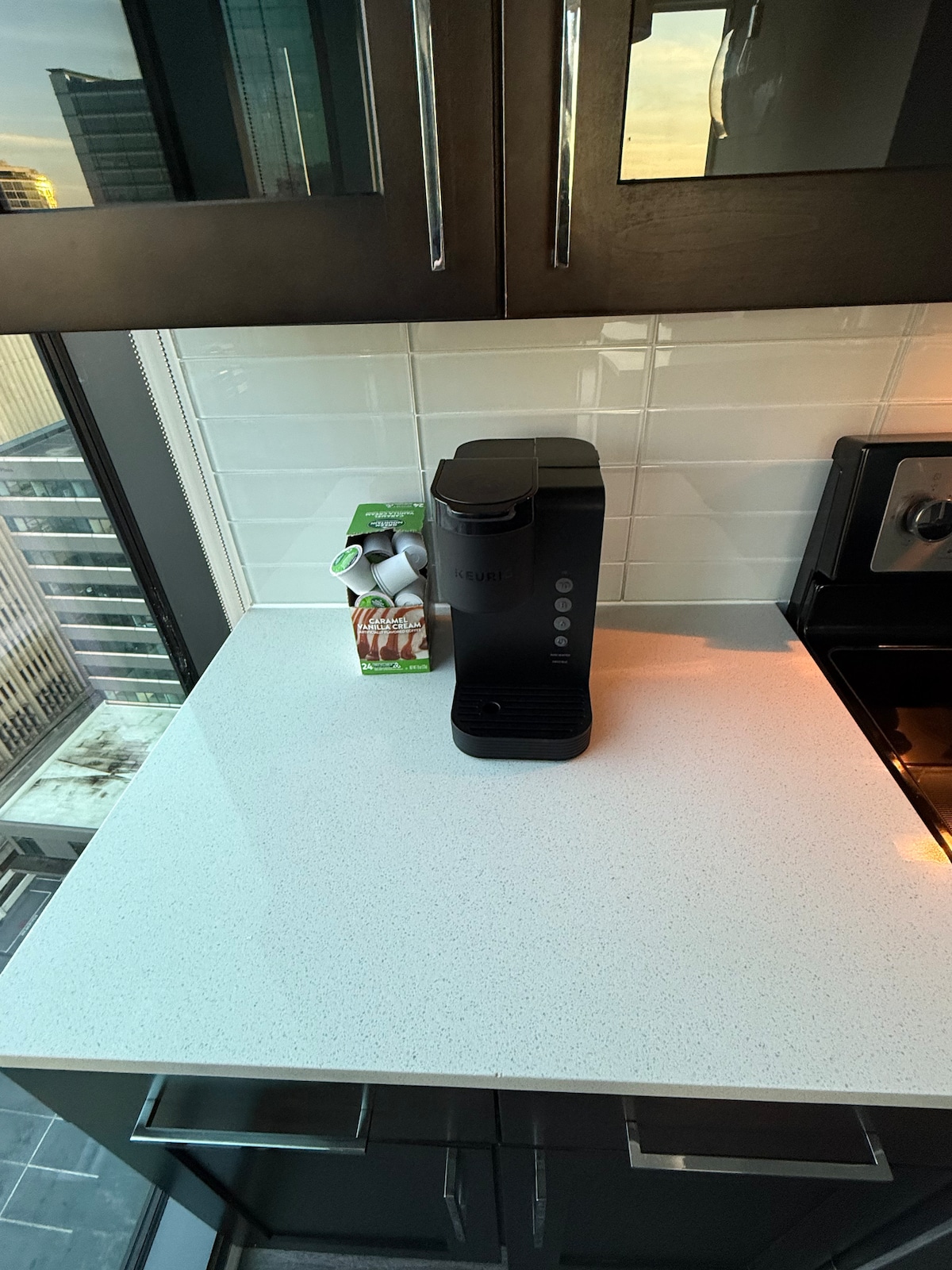 A sleek kitchen countertop is displayed, featuring a coffee machine and a carton of milk alongside several creamers. The modern cabinetry and large windows allow for ample natural light, highlighting the clean lines and functionality of the space.