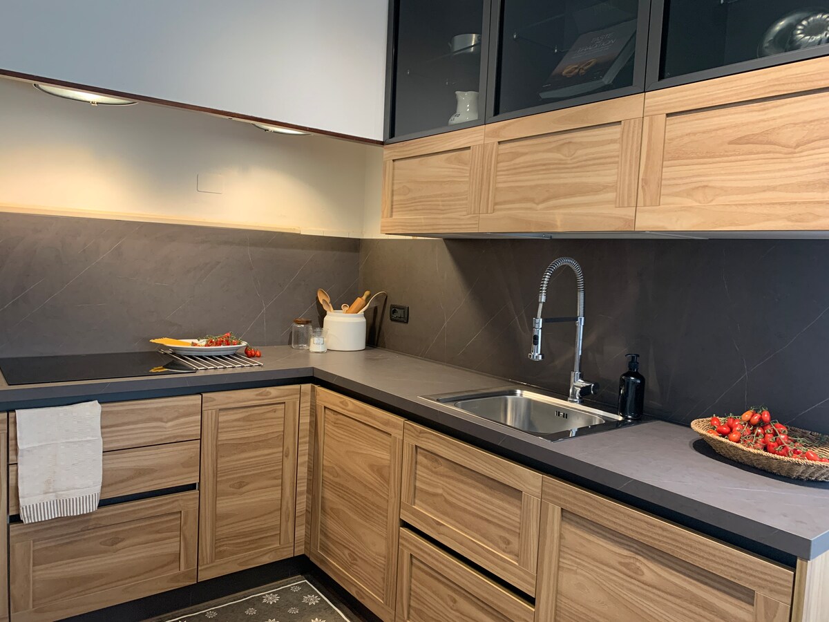 The kitchen features modern wooden cabinetry with a dark countertop. A sink and faucet are positioned conveniently, and a range of utensils is organized nearby. Fresh strawberries are displayed on a round plate, adding a touch of color to the space. Ample storage and workspace are evident.