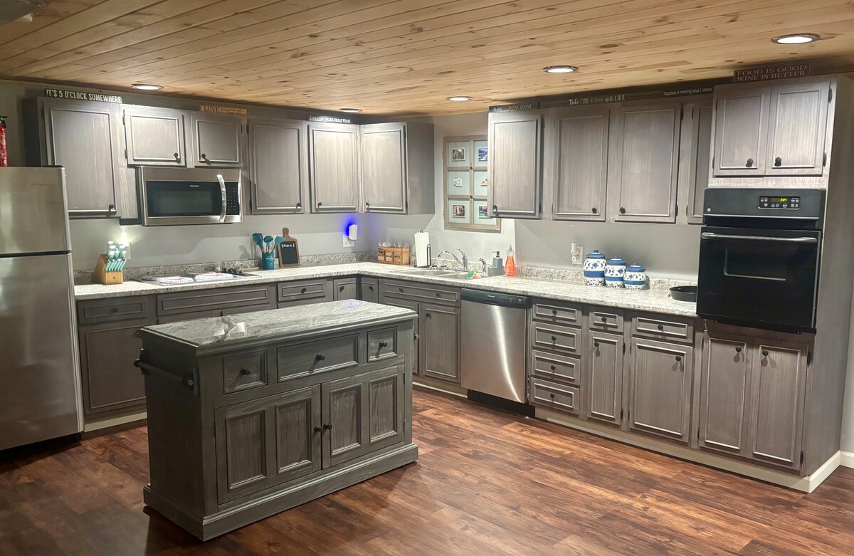 A functional kitchen is equipped with modern appliances, including a refrigerator, microwave, and dishwasher. The light-colored cabinetry contrasts with the dark wood flooring. A central island provides additional workspace, illuminated by recessed lighting overhead, contributing to a bright and inviting cooking environment.