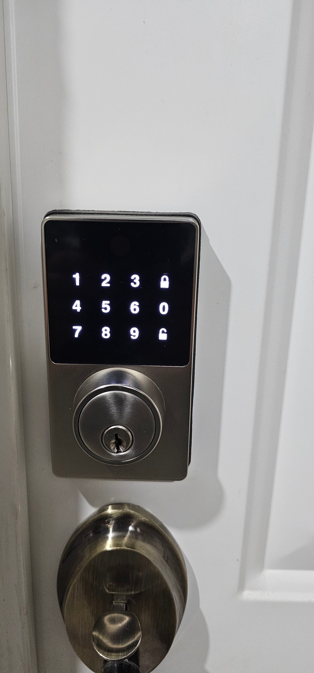 A sleek digital lock is mounted on a white door, featuring a numeric keypad illuminated in white. The keyhole is situated beneath the keypad, surrounded by a brushed metal finish, emphasizing a modern and secure entrance.