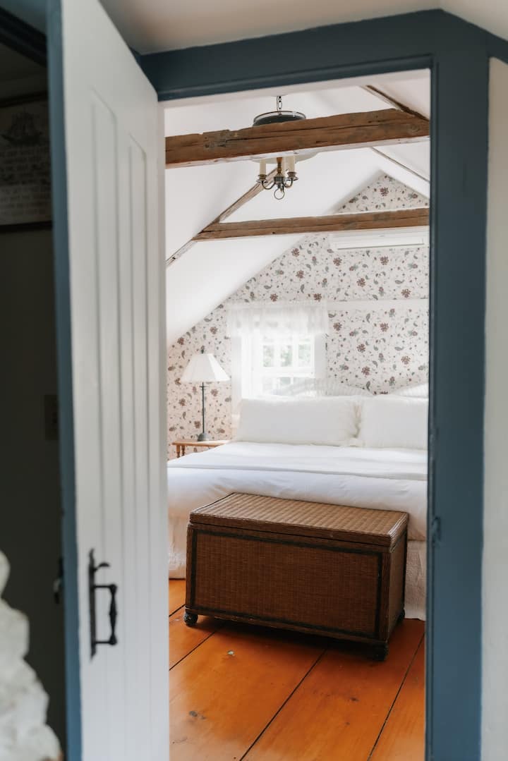A charming king bedroom in the eaves with beautiful beams offering a welcoming, homey atmosphere.