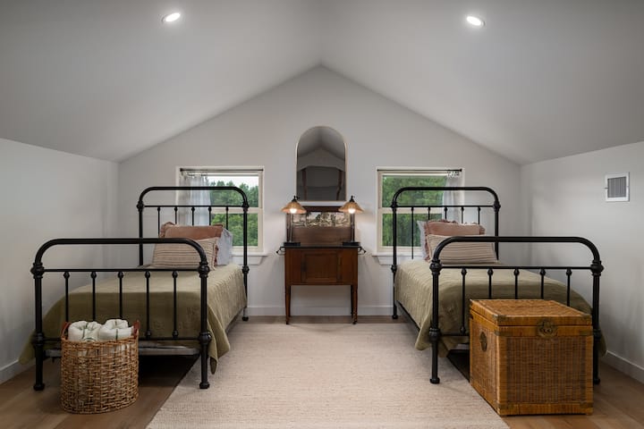 The loft features two twin beds with vintage iron frames and soft linens — a cozy retreat for kids or extra guests.