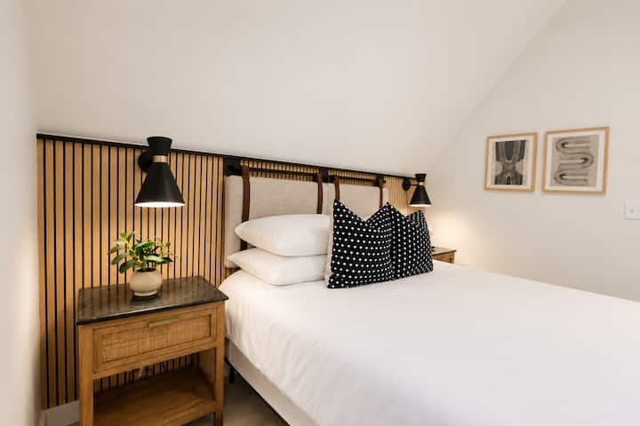 This stylish bedroom features a queen bed, cozy bedding, blackout shades, and vaulted ceilings.