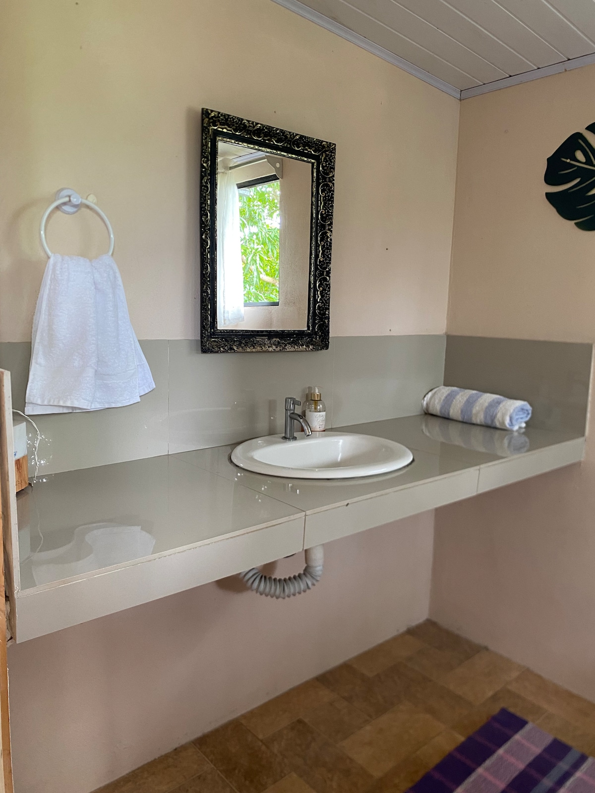 A well-lit bathroom area features a sleek sink mounted on a polished countertop. A large mirror is framed with an ornate design. A neatly arranged towel hangs beside the sink, and a rolled towel rests nearby, adding functional touches to the space.