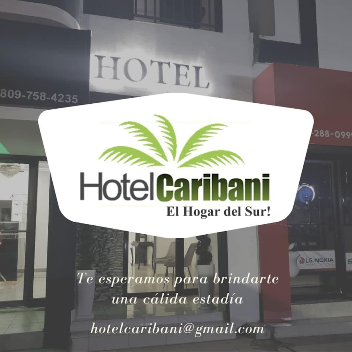 The hotel entrance showcases a bright and clear sign featuring the name 'Hotel Caribani' alongside palm tree graphics. Neon lighting highlights the inviting façade, while contact information is displayed at the bottom, promoting a warm welcome for guests.