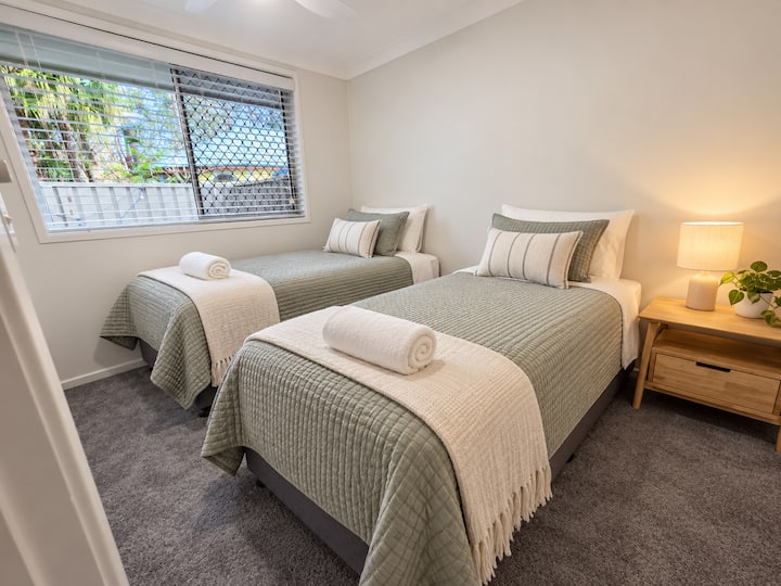 Comfortable second bedroom with two single beds, soft coastal styling and natural light.