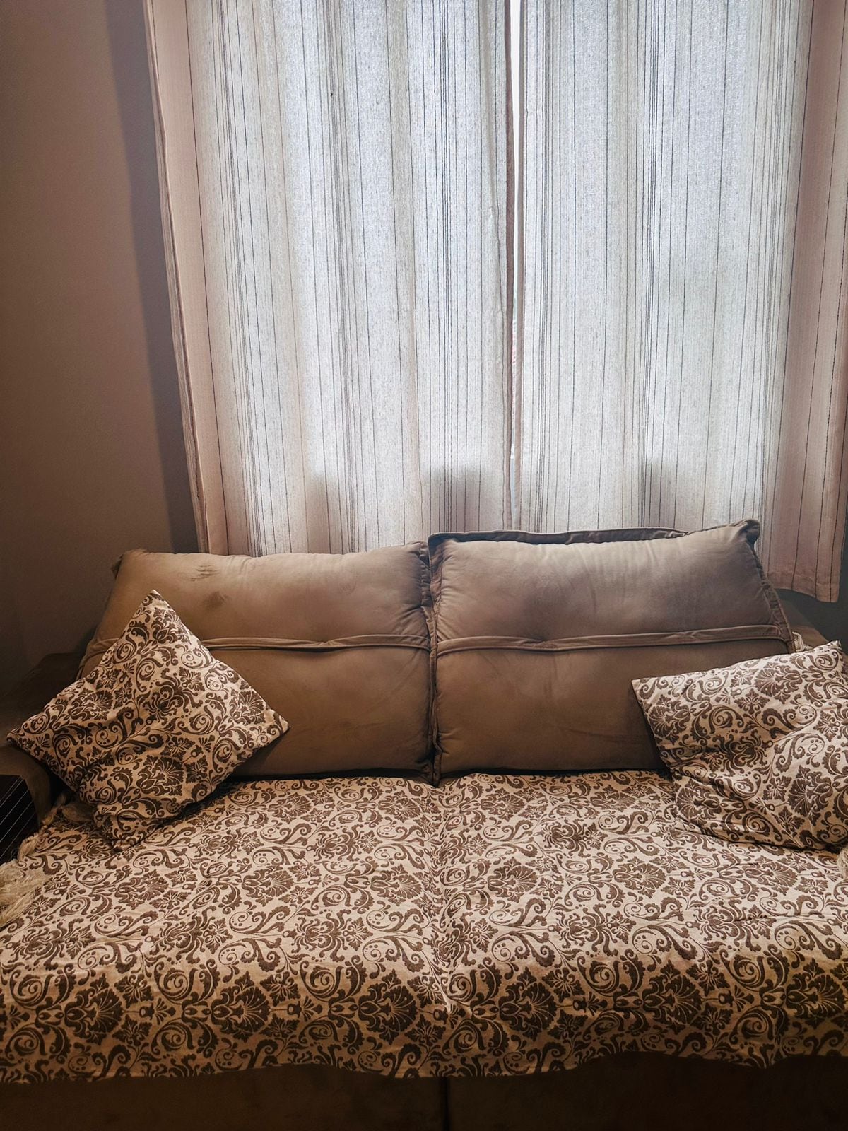 A comfortable couch is adorned with decorative pillows and a patterned throw. Sunlight filters through sheer curtains, creating a soft and inviting ambiance. The arrangement encourages relaxation and offers a nice spot for unwinding.