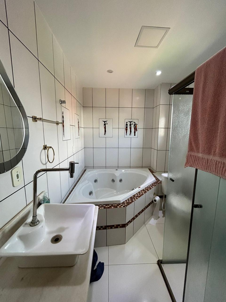 The bathroom features a modern design with sleek tiles and a spacious jetted tub surrounded by a decorative border. A clear glass shower enclosure is present alongside a contemporary sink with a mirror above. Soft lighting highlights the clean, inviting atmosphere.