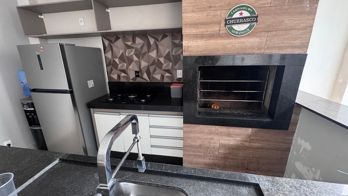 The kitchen area features modern cabinetry with a textured wall design. Stainless steel appliances, including a refrigerator and a gas stove, complement the dark countertops. A built-in grill is integrated into the cabinetry, enhancing the cooking space.