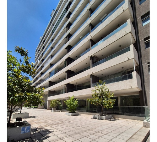 A modern apartment building is depicted with six floors and multiple balconies that overlook a landscaped outdoor area. Trees are positioned along the paved walkway, creating a sense of greenery. Smooth surfaces and a well-maintained facade contribute to the building's inviting appearance.