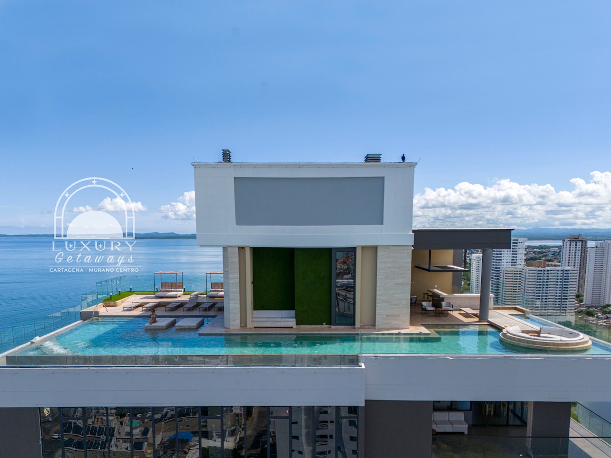 The rooftop infinity pool, perched on the 30th floor, offers expansive views of the ocean and city skyline. A sleek lounge area is visible beside the pool, complemented by modern furnishings and a jacuzzi, all surrounded by the stunning backdrop of Cartagena's coastline.