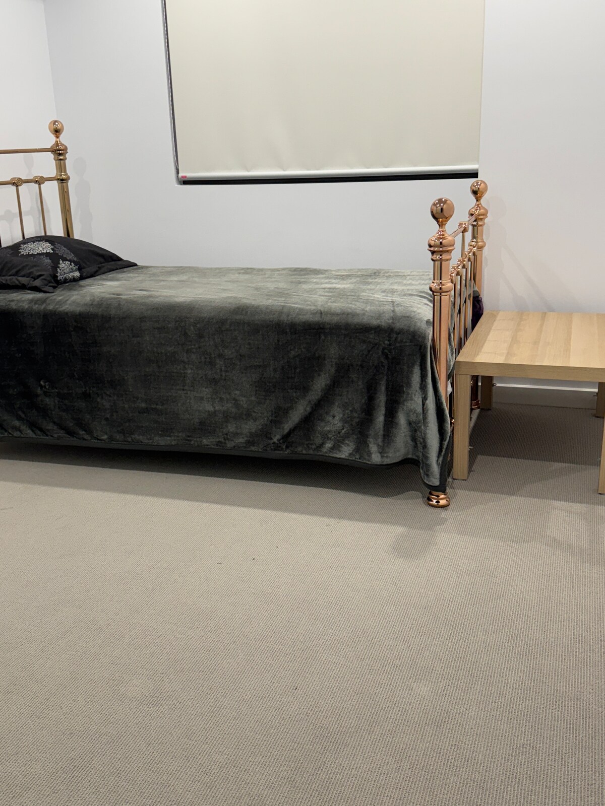 A sleeping area is shown, featuring a spacious bed with a dark gray plush blanket. The bed frame is metallic, and a small wooden nightstand is positioned beside it. A light-colored carpet covers the floor, creating a calm atmosphere.