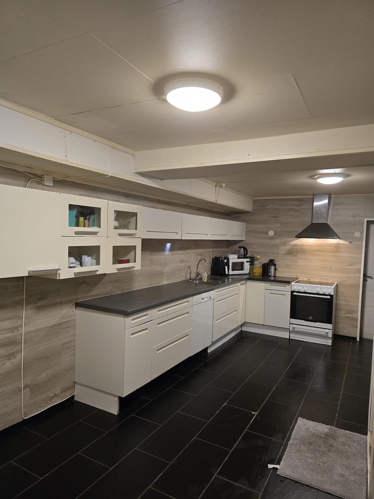 A modern kitchen is showcased, featuring sleek cabinetry and a dark countertop. Stainless steel appliances are arranged for convenience, including a microwave and coffee maker. Under-cabinet lighting enhances the space, while a light-colored tile backsplash complements the overall design.