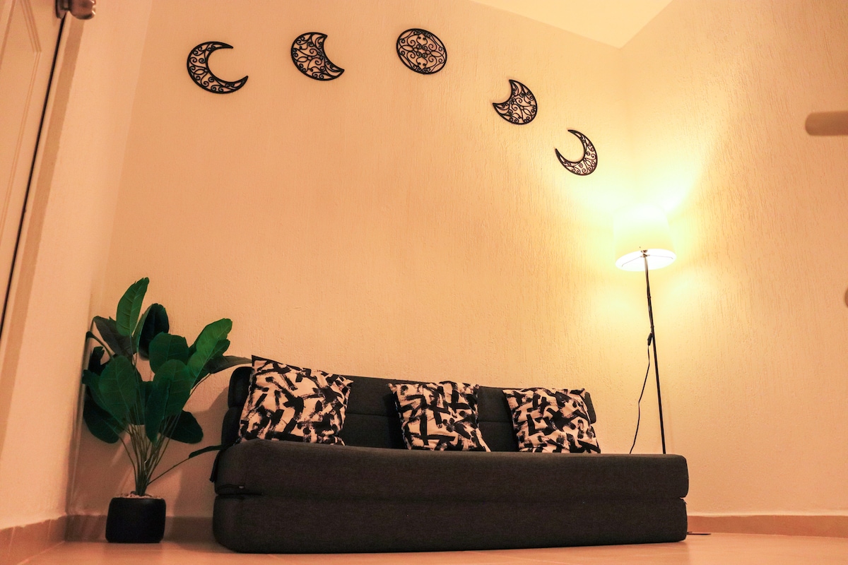 زاوية مريحة مع أريكة وإضاءة دافئة وزخرفة من القمر. مثالية للاسترخاء والاستمتاع بجو هادئ وبسيط.
