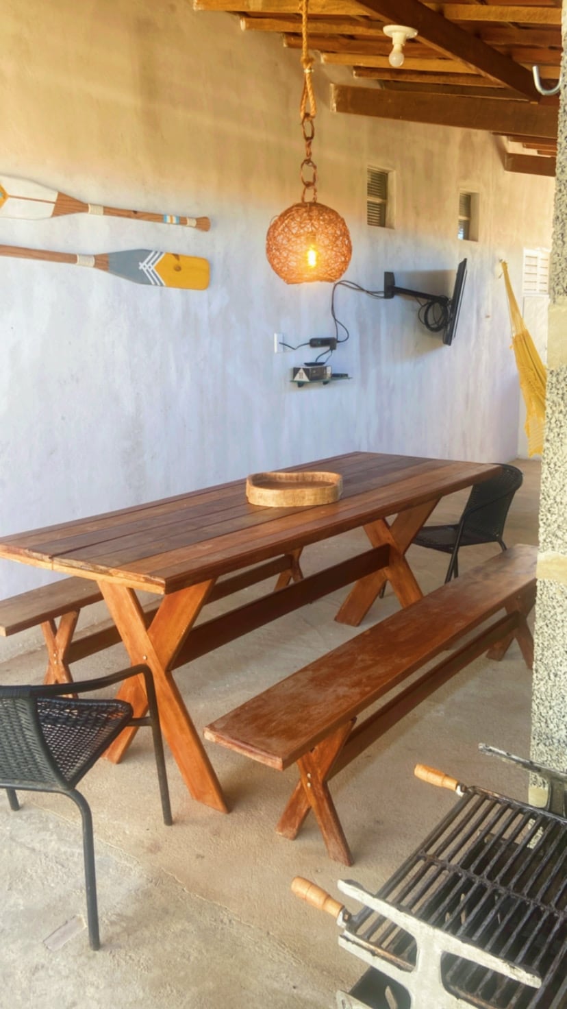 An outdoor dining area is presented with a wooden table and two matching benches. A woven pendant light hangs above the table, and black chairs are positioned at each end. Decorative oars are displayed on the wall, contributing to a relaxed ambiance.