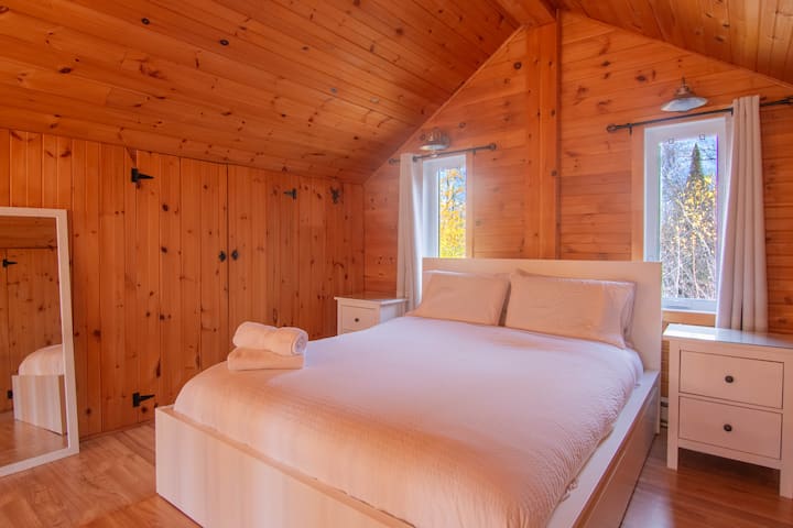 Spacious master bedroom with a queen bed and large windows providing beautiful natural light. Warm wood décor and comfortable bedding for peaceful nights.