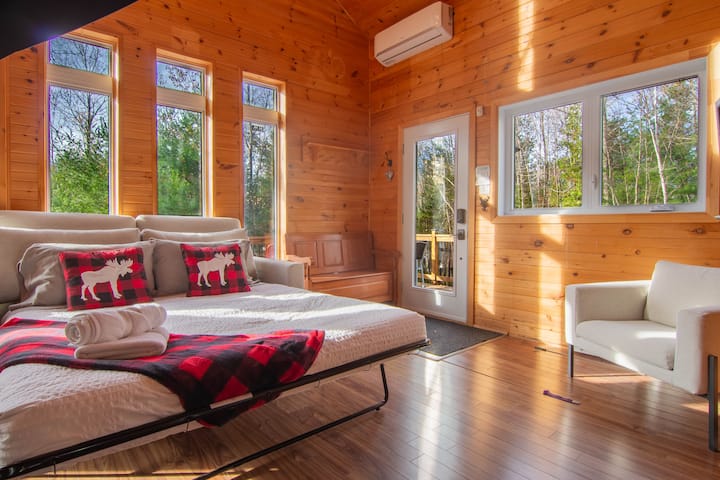 A bright and calming space with large windows offering a direct view of the forest. This warm living room in natural wood invites relaxation, with its comfortable sofa and chalet-style cushions.