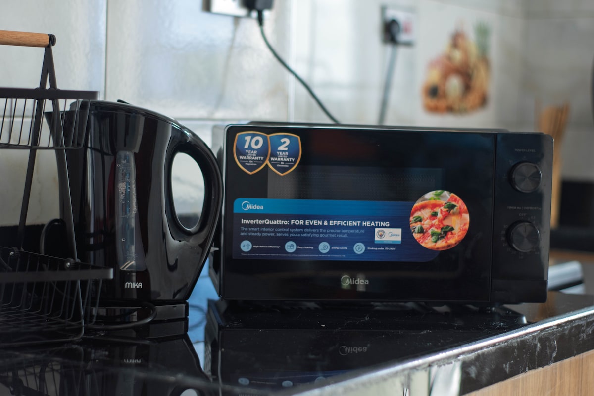 A modern kitchen countertop is showcased featuring a sleek microwave with a digital display, positioned beside a contemporary kettle. The surface is smooth and dark, highlighting the appliances against a light-colored backsplash.