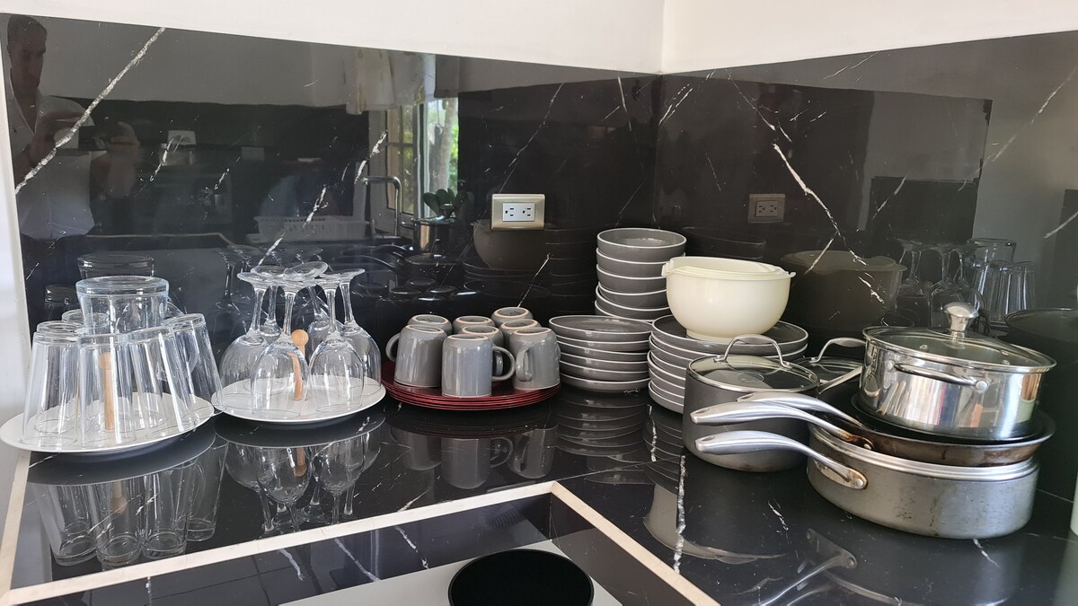 A neatly arranged kitchen countertop features various glassware, including wine glasses and coffee mugs, complemented by a set of bowls and plates. Two stainless steel pots are positioned near the edge, creating an organized cooking area against a sleek black marble backdrop.