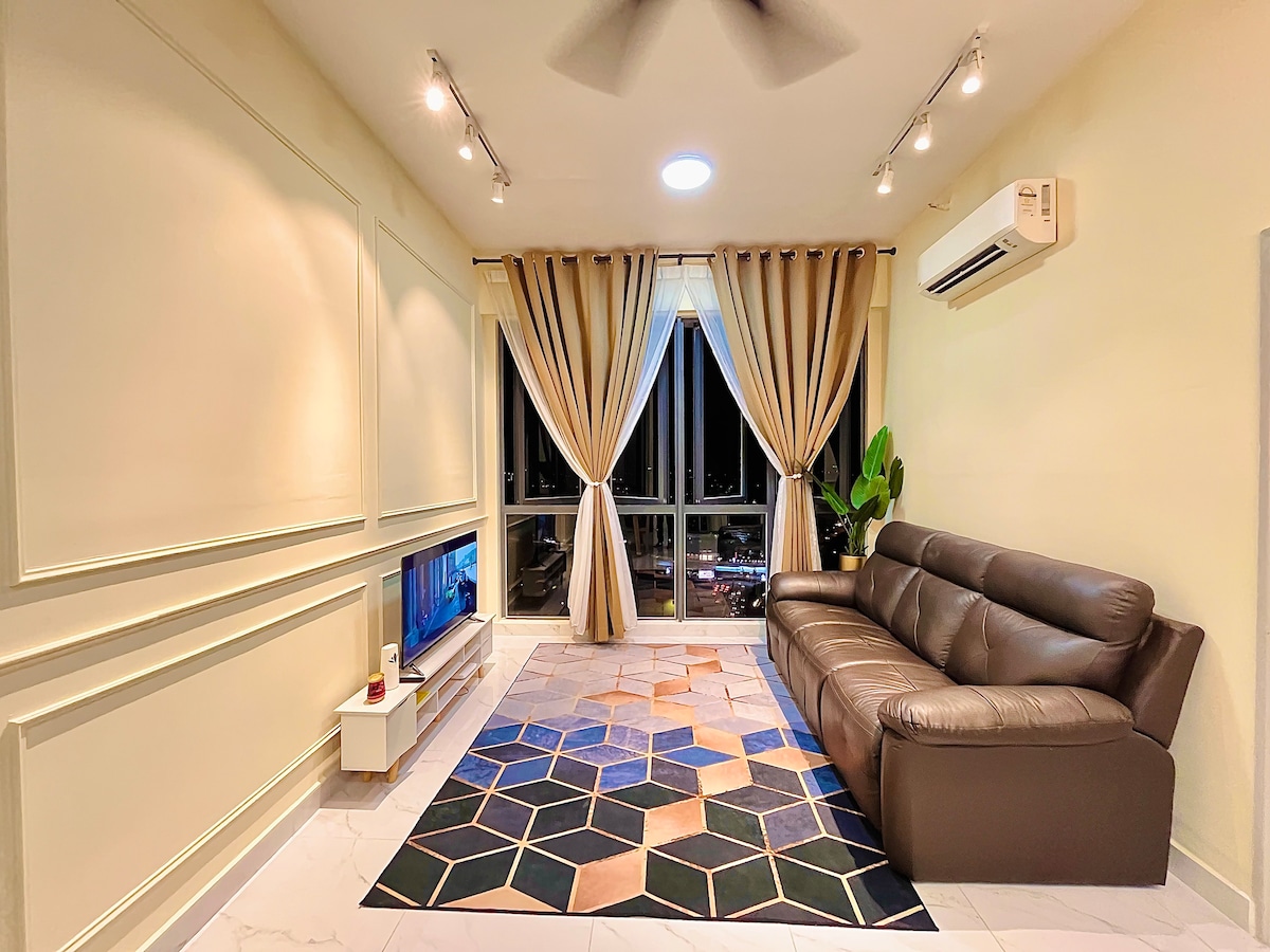 A modern living area features a large, dark leather sofa facing a mounted television. A geometric-patterned rug adds color to the space, while floor-to-ceiling windows are elegantly framed by light-colored drapes. Indoor plants bring a touch of greenery to the atmosphere.