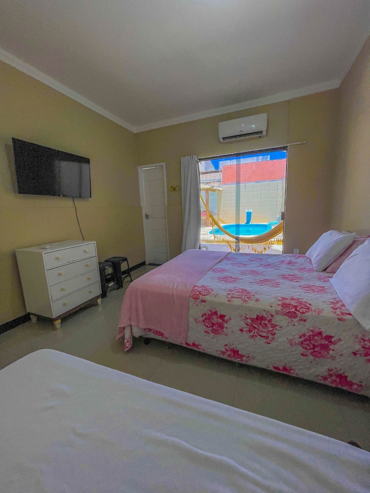 Spavaća soba s TV-om, klima-uređajem, električnim tušem i balkonom s visećom ležaljkom.