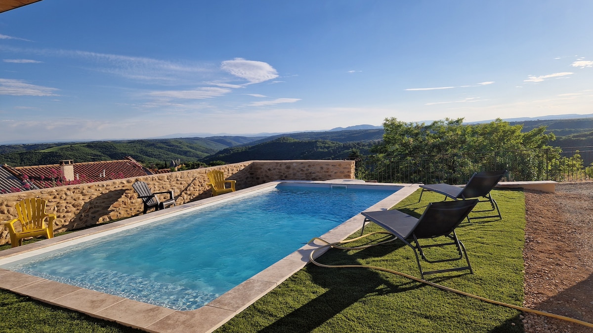 A private pool is featured in a serene outdoor setting, surrounded by lush greenery and offering panoramic views of the surrounding hills. Two lounge chairs are positioned beside the water, ready for relaxation under the clear blue sky.