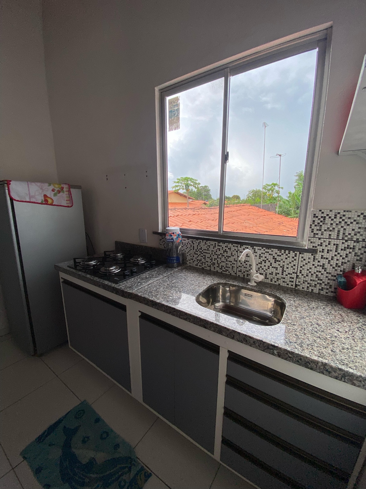 A functional kitchen area is equipped with a modern gas stove and a spacious sink. Natural light floods through a large window, showcasing views of the outdoors. A refrigerator is placed within easy reach, contributing to the kitchen's efficient layout.