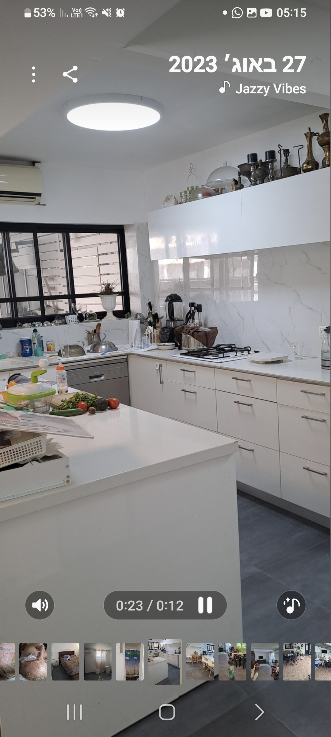 A modern kitchen is presented, featuring white cabinetry and a spacious countertop. Kitchen appliances, including a stovetop and kettle, are visible. Natural light enters through a window, illuminating the area. A selection of fresh fruits is arranged, enhancing the inviting environment.