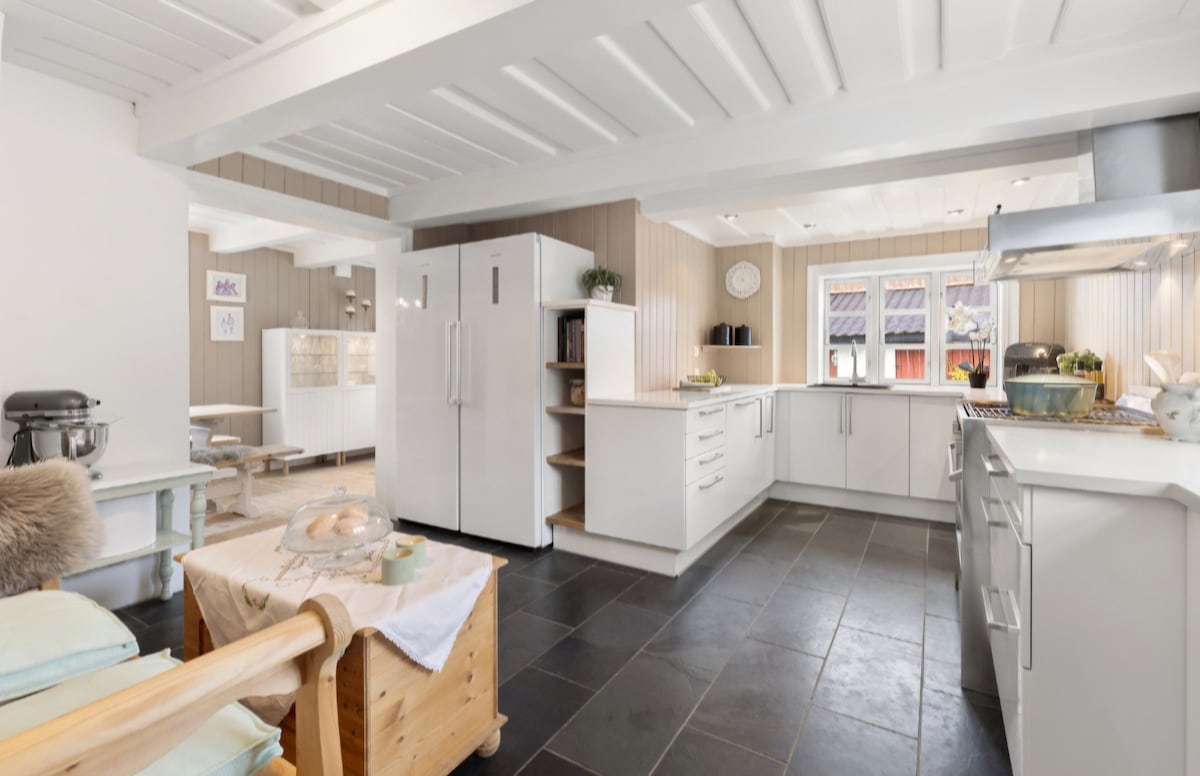 A spacious kitchen showcases modern white cabinetry and appliances, with a large refrigerator and a well-organized countertop. Natural light enhances the area, flowing through multiple windows. Slate tile flooring is featured, providing a clean and functional workspace.